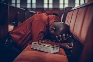 Man kneeling in church praying with bible about LGBT+ parade.